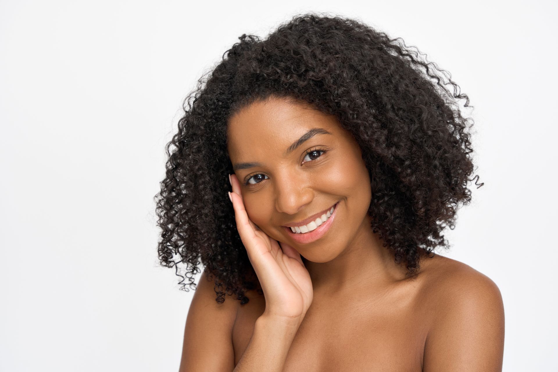 Smiling woman with curly hair resting a hand against her cheek