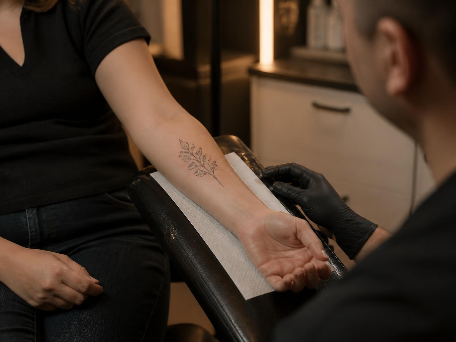 Clinician examining a small botanical forearm tattoo