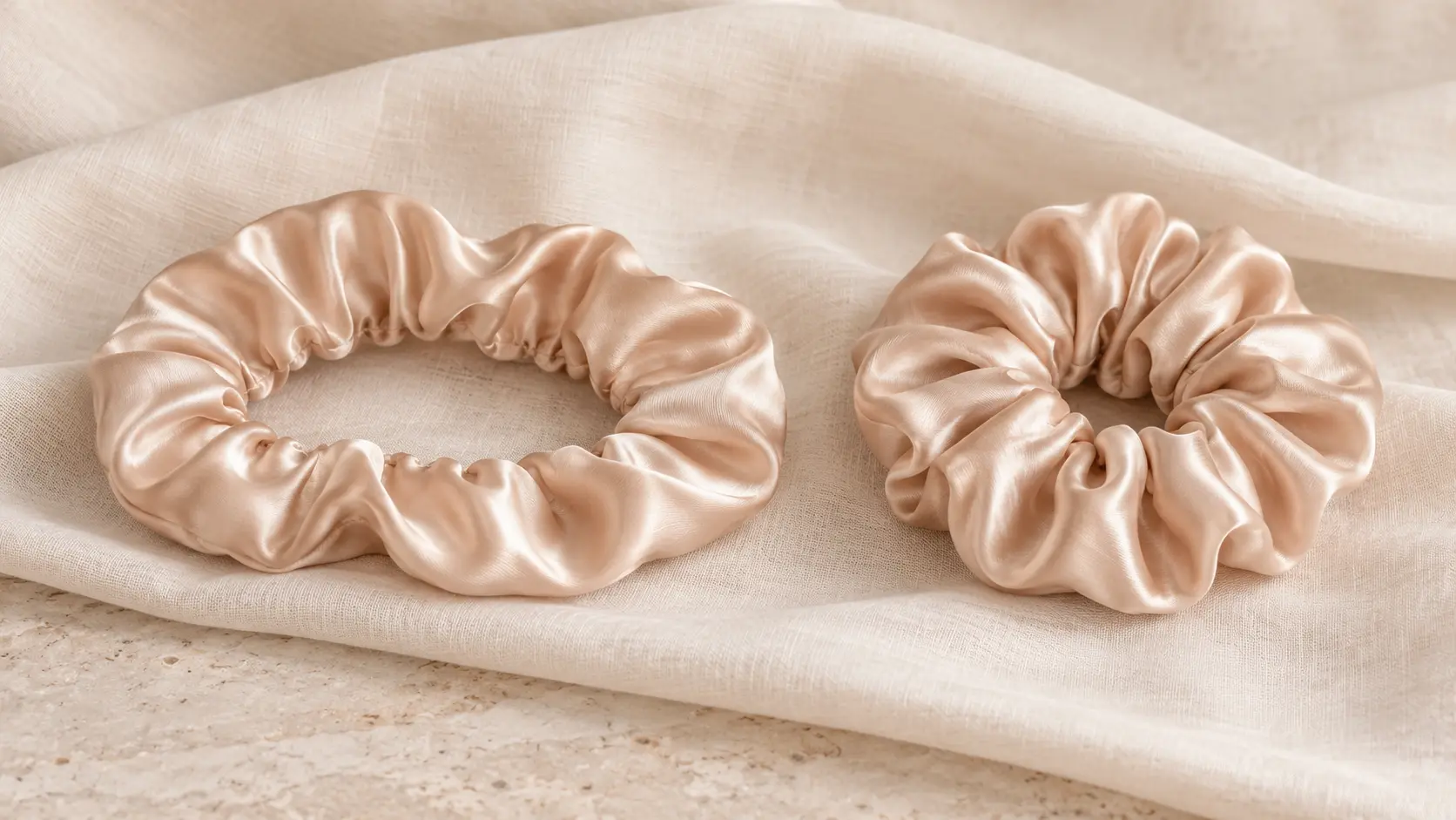 Two champagne silk scrunchies resting on soft linen, one gently extended and relaxed, the other more gathered, used as an analogy for tissue elasticity